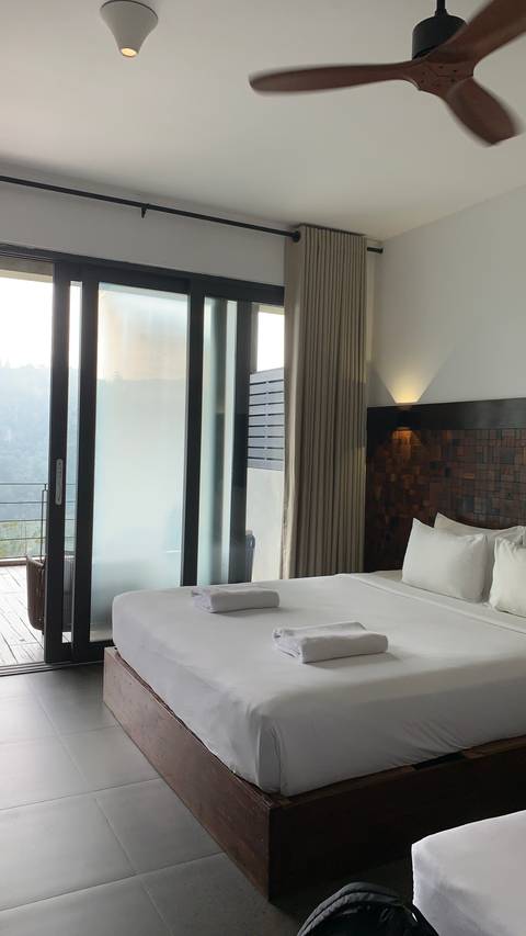       Modern hotel room with neatly made bed and balcony doors overlooking a misty valley
  