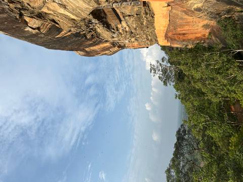       Dramatic orange rock face of Sigiriya rising above lush jungle under a blue sky
  