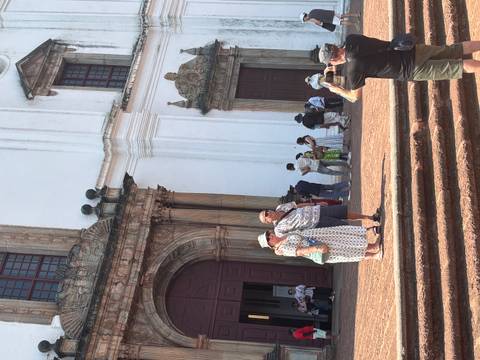       Tourists posing for photos outside historic white basilica with ornate doorway
  
