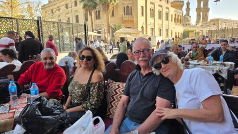       Four travelers relaxing at an outdoor cafe in historic Cairo with ornate buildings and mosque minarets in the background.
  