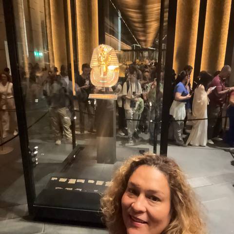       Museum selfie featuring the iconic golden funerary mask of Tutankhamun behind protective glass with crowds reflected.
  