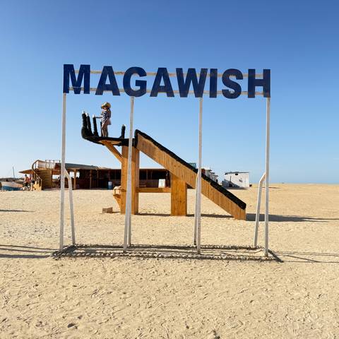       Tall metal frame sign reading 'MAGAWISH' standing in a barren sandy landscape at a Red Sea resort.
  