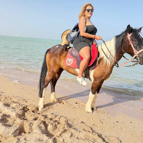       Woman riding a brown and white horse along the shallow surf of a quiet Red Sea beach.
  