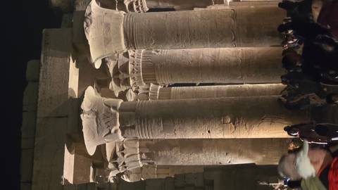       Nighttime view of illuminated columns inside Kom Ombo Temple crowded with visitors
  