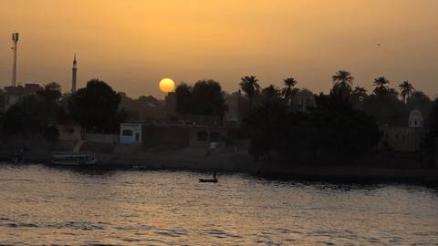       Sunset over Nile River with silhouetted palm trees and village buildings
  