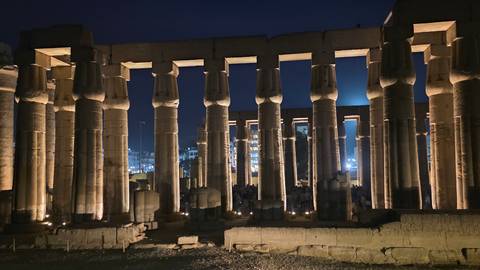       Night view of illuminated sandstone columns and architraves at an ancient Egyptian temple courtyard
  