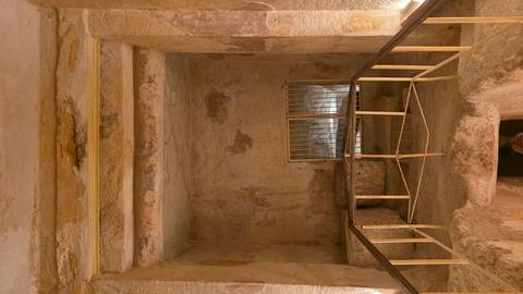       Interior of an ancient stone tomb chamber with gated recess and faded wall paintings
  