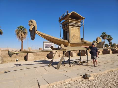       Traveller points at a large gilded ceremonial bark statue displayed outdoors under blue sky
  