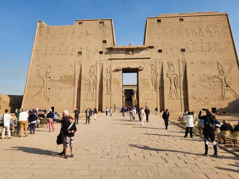       Crowds entering the monumental pylon entrance of Edfu Temple adorned with hieroglyphic reliefs
  