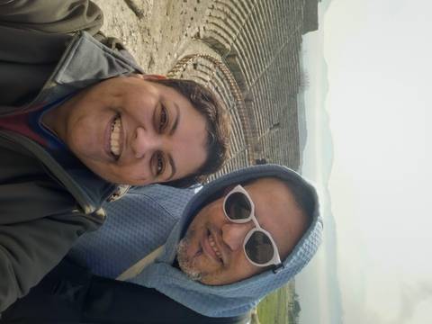       Smiling couple selfie overlooking the stone tiers of an ancient amphitheatre.
  