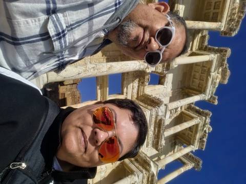       Close-up selfie of travellers with the ornate façade of the Celsus Library rising behind.
  