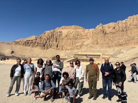       Tour group posing in front of the terraced facade of Hatshepsut Temple set against rugged desert cliffs.
  