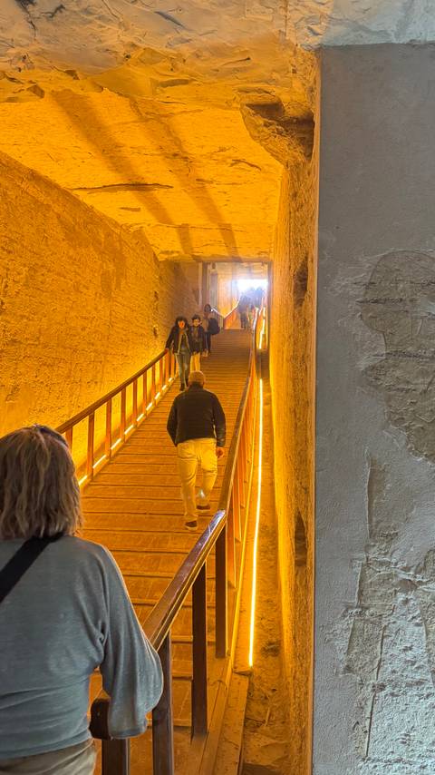       Visitors climb a warmly lit stair tunnel inside an ancient Egyptian monument.
  