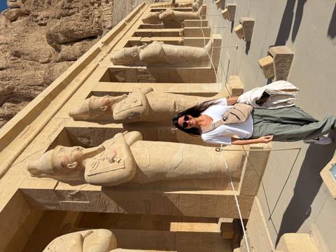       Female traveller stands in front of massive sandstone statues carved into an Egyptian temple facade.
  