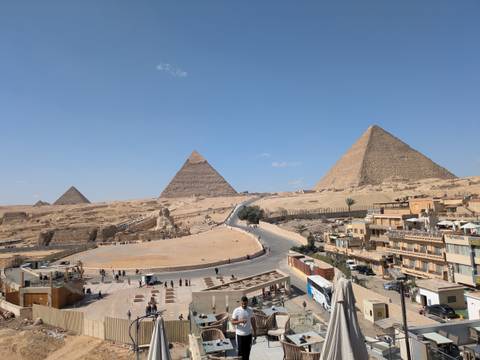       Iconic Great Pyramids of Giza rise above desert sands under clear blue sky with scattered visitors below.
  