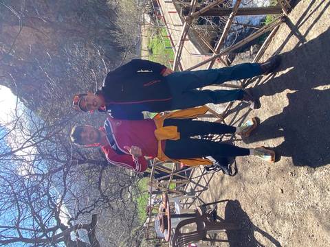       Two hikers pose on a sunny mountain trail with bare trees and rocky peaks in the Atlas Mountains.
  