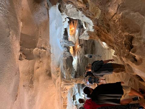       Visitors explore a limestone cave with stalactites and illuminated chambers along a rough path.
  