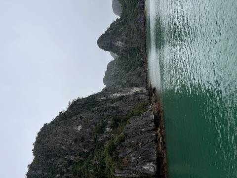       Emerald green water surrounded by dramatic limestone karst cliffs and rocky shoreline
  