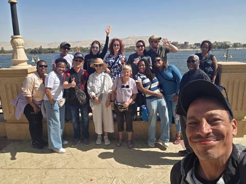       Duplicate group photo by riverside promenade and desert backdrop.
  