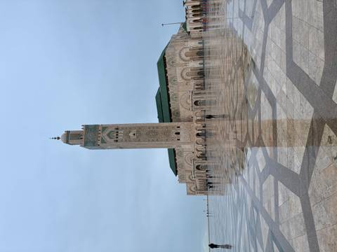       Vast esplanade reflecting Hassan II Mosque and its towering minaret after rain.
  