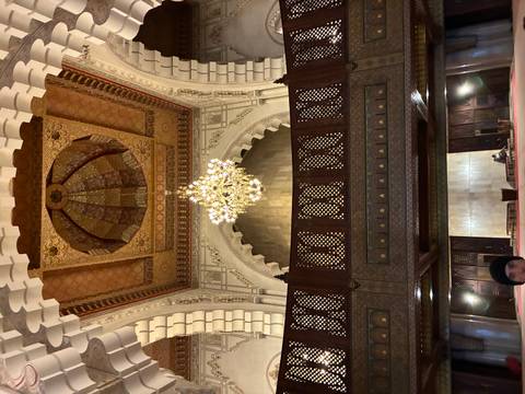       Lavishly decorated mosque interior with grand chandelier and carved wooden gallery.
  