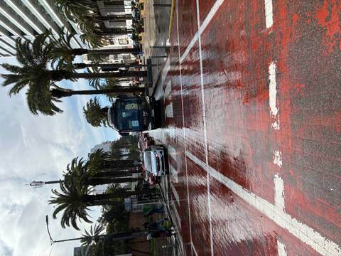       Rain-soaked street with tour bus and palm trees reflecting on red pavement.
  