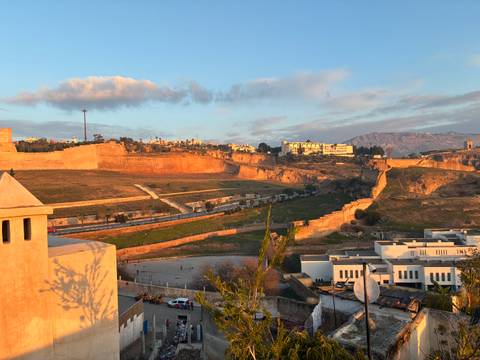      Sunset view across ancient fortified walls and hills surrounding a Moroccan city with warm golden light
  