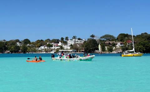       Kayaks and small tour boats float on the brilliant turquoise waters of Bacalar Lagoon with villas and palms in the distance.
  