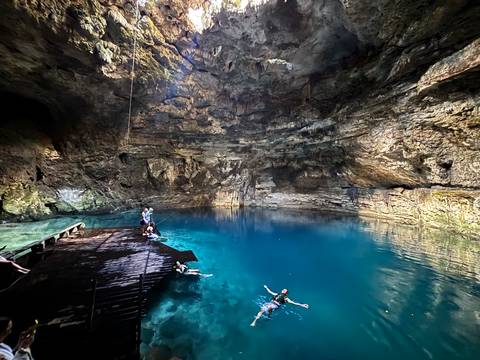       Visitors swim and relax in the crystal-clear blue waters of a dramatic underground cenote.
  