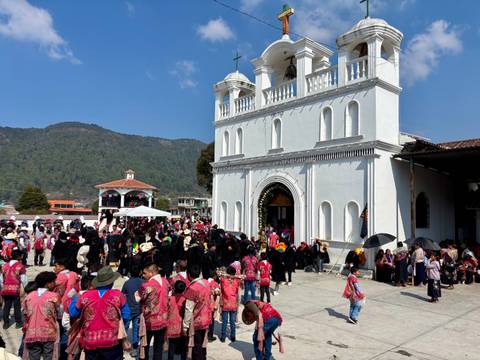       Large crowd in traditional dress gathers outside a white church during a vibrant highland festival.
  