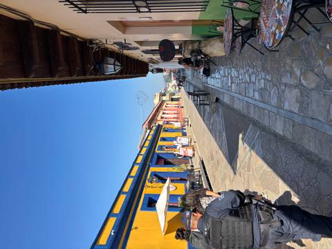       Colorful colonial street in San Cristóbal de las Casas lined with cafés and pedestrians on a clear morning.
  
