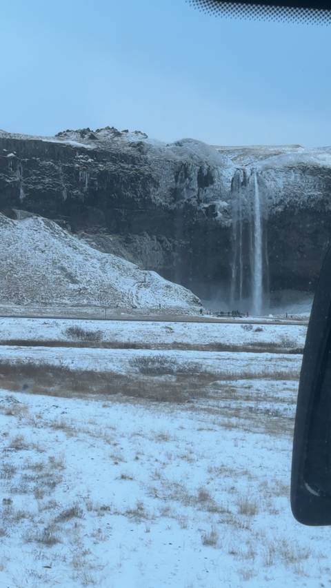       Distant view of a tall waterfall plunging over an icy cliffside in winter conditions.
  