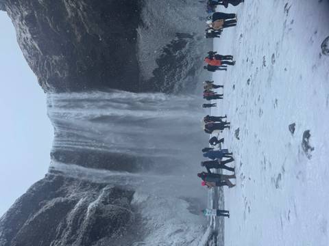       Visitors wearing winter gear stand before a powerful waterfall cascading into a snowy basin.
  