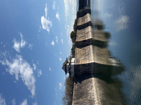       Moat and high stone walls reflecting in still water below a small white watchtower under a blue sky.
  