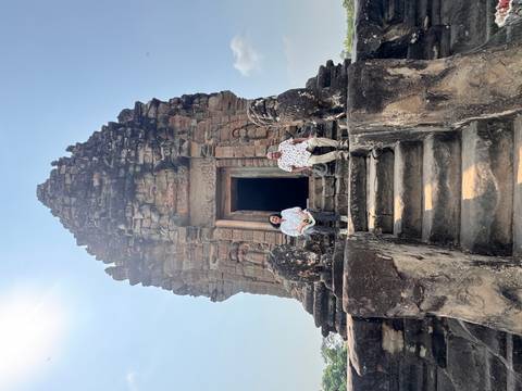       Couple sitting on stone steps of a small ancient Khmer temple tower against a clear blue sky.
  