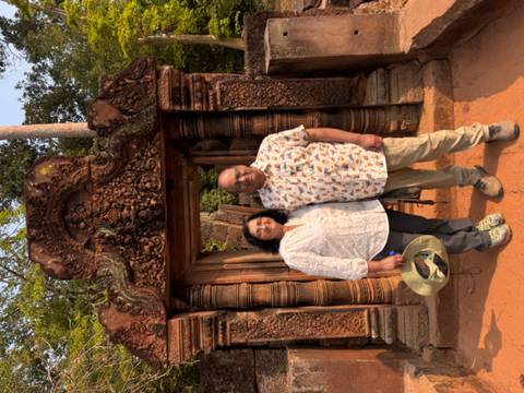       Couple standing in an ornate red-sandstone doorway richly carved at Banteay Srei temple.
  