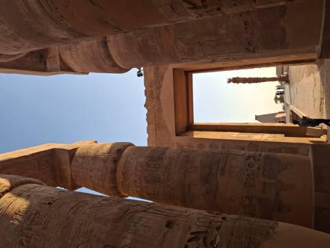       Tall engraved sandstone columns framing a doorway that looks out toward an obelisk and palm in an ancient Egyptian temple.
  