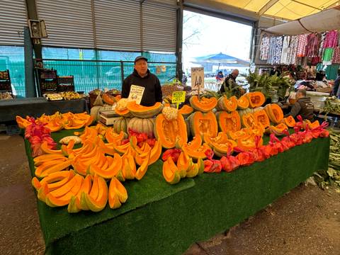       Market vendor stands behind an abundant display of sliced bright orange pumpkins at an indoor bazaar.
  