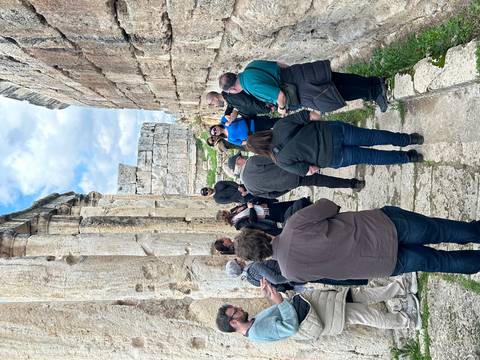       Tour group listens to a guide while standing between towering ancient limestone columns and ruins.
  