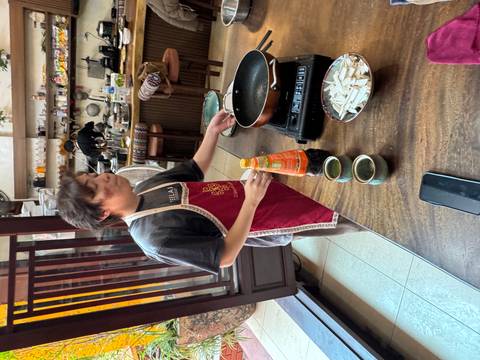       Cooking class instructor wearing an apron stirring ingredients in a pan inside a homely kitchen studio.
  