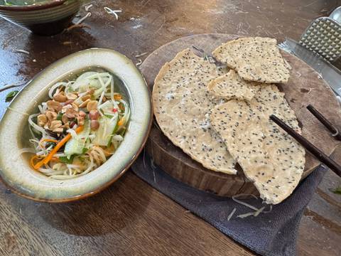       Overhead view of fresh salad with chopped peanuts and broken sesame crackers on a wooden board.
  
