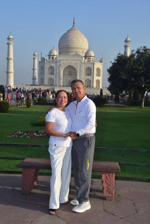       Couple posing hand in hand on the Taj Mahal gardens with the monument towering behind.
  