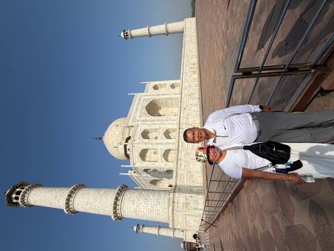       Couple smiling beside a Taj Mahal minaret under a deep blue sky.
  