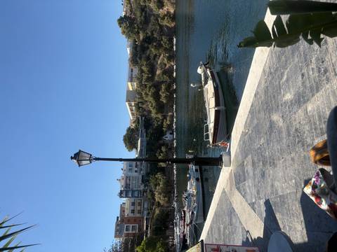       Small fishing boats float on a tranquil harbour beside a classic lamppost under a clear blue sky.
  
