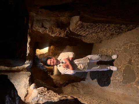       Person stands in a narrow, dimly lit stone passageway inside an ancient pyramid.
  
