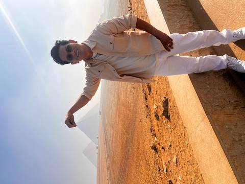       Tourist pretends to pinch the distant pyramid from a sandy overlook.
  