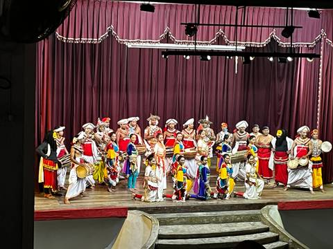       Traditional Kandyan dance troupe in vibrant costumes take a group bow on theatre stage.
  
