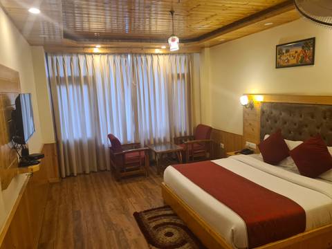       Cozy hotel room with a double bed, red accents, wood paneling and large curtained window.
  