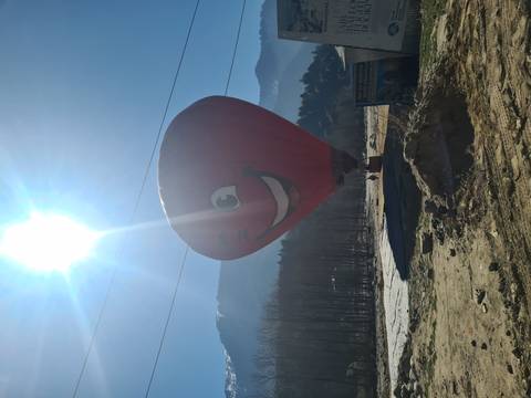      Red smiling hot-air balloon on a sunny morning with snowy peaks in the distance.
  