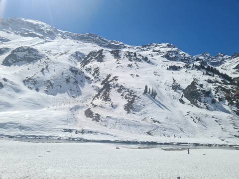       Expansive snowy mountain slope with jagged peaks and a frozen river under clear blue sky.
  
